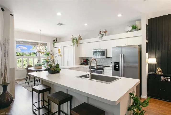 Kitchen featuring white cabinets, appliances with stainless steel finishes, wood finished floors, decorative light fixtures, and decorative backsplash