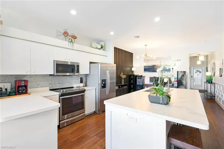 Kitchen with stainless steel appliances, tasteful backsplash, dark wood-type flooring, and a center island with sink