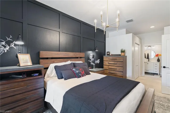 Bedroom featuring a chandelier, visible vents, light colored carpet, and connected bathroom