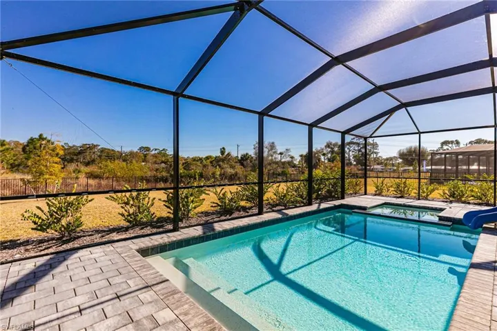 Swimming pool with a sunroom, glass enclosure, a jacuzzi, a water slide, and a patio