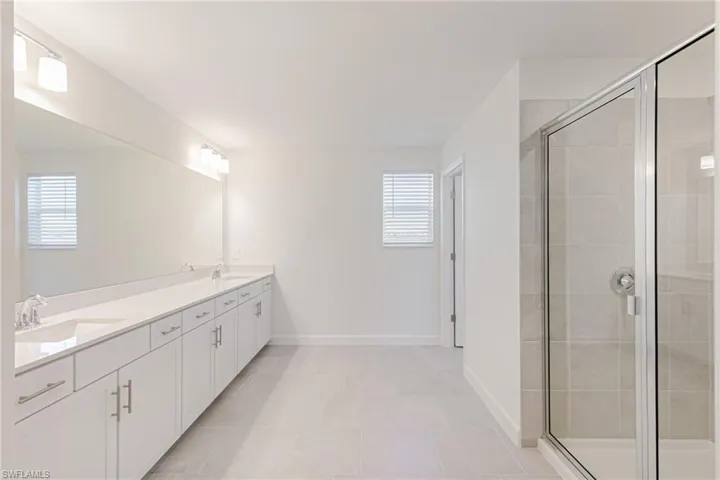 Bathroom featuring a shower stall, double vanity, and light tile patterned floors