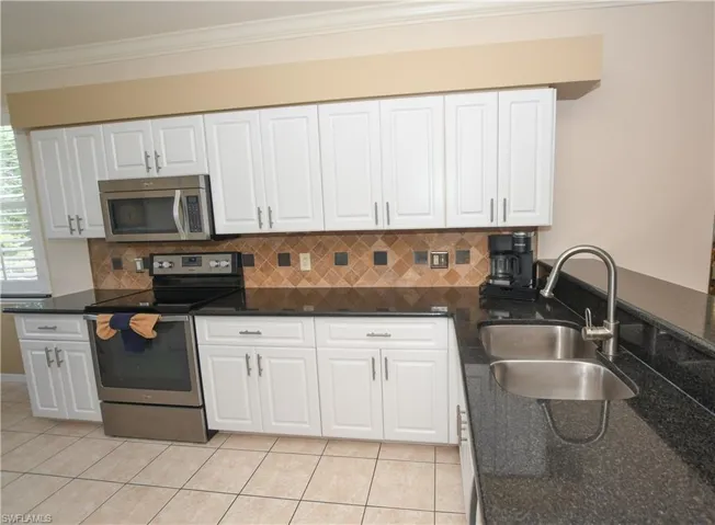 Kitchen featuring white cabinets, crown molding, appliances with stainless steel finishes, a sink, and light tile patterned floors