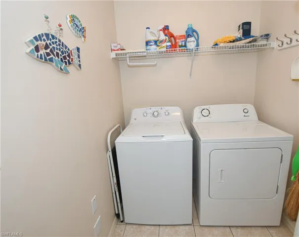 Clothes washing area featuring light tile patterned flooring, washing machine and dryer, and laundry area