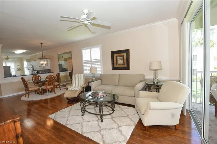 Living room with dark wood finished floors, ceiling fan with notable chandelier, and crown molding