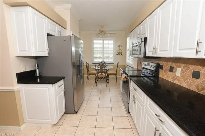 Kitchen featuring white cabinets, ornamental molding, stainless steel appliances, dark countertops, and light tile patterned floors