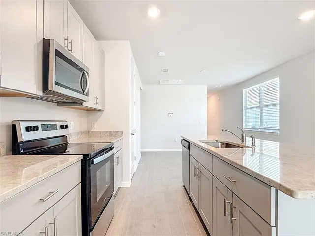 Kitchen with appliances with stainless steel finishes, light wood-style flooring, light stone counters, a kitchen island with sink, and recessed lighting