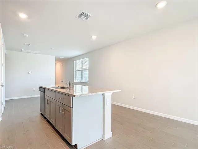 Kitchen featuring a center island with sink, light wood-style floors, light stone countertops, gray cabinetry, and recessed lighting