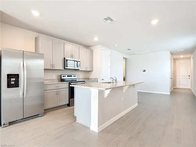 Kitchen featuring stainless steel appliances, light stone counters, wood tiled floors, a kitchen bar, and recessed lighting