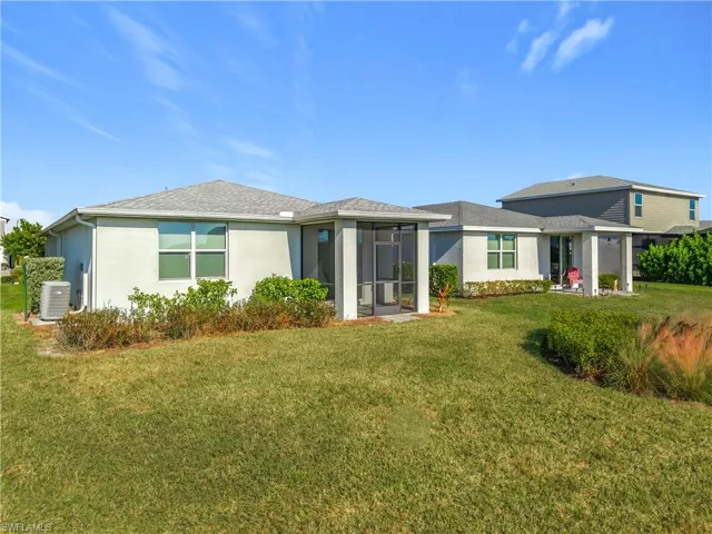 Rear view of property with a yard, stucco siding, a sunroom, and roof with shingles