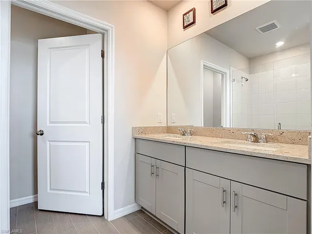 Full bath with double vanity, wood tiled floors, and a tile shower