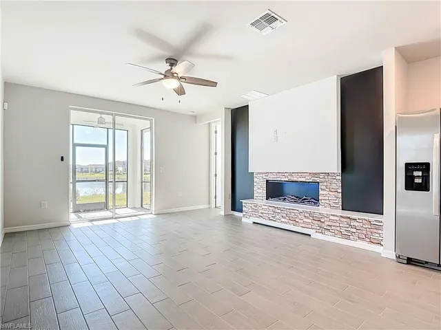 Unfurnished living room featuring ceiling fan, wood tiled floors, a stone fireplace, and a water view