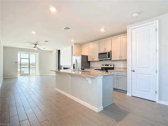 Kitchen with a kitchen bar, stainless steel appliances, ceiling fan, light wood-style flooring, and a center island with sink