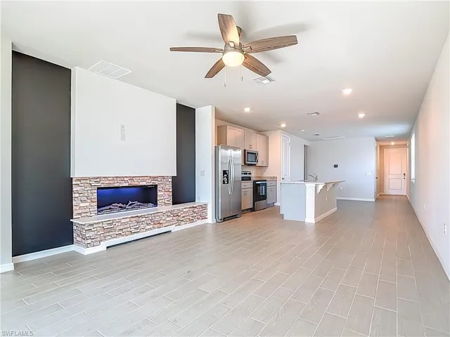 Unfurnished living room with ceiling fan, recessed lighting, wood finish floors, and a stone fireplace