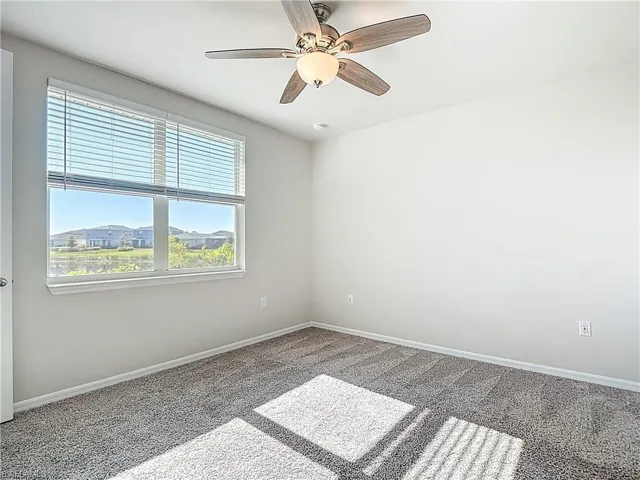 Carpeted spare room featuring baseboards and ceiling fan