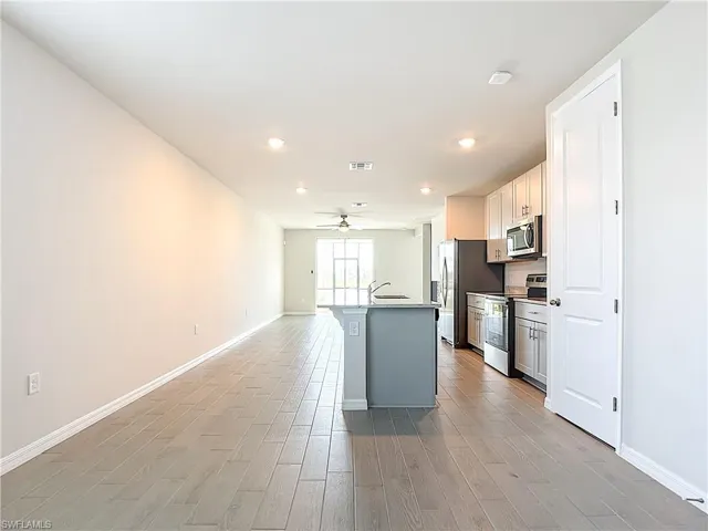 Kitchen with stainless steel appliances, an island with sink, light wood-style flooring, white cabinets, and recessed lighting