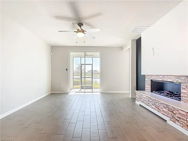 Unfurnished living room with wood tiled floors, a ceiling fan, and a stone fireplace