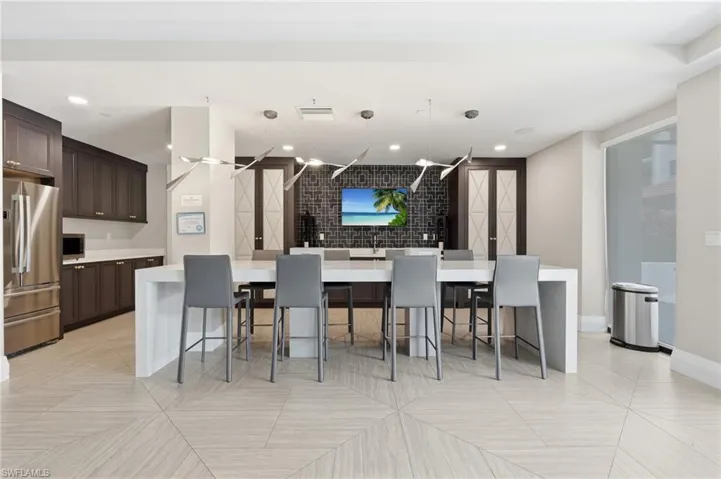 Spacious common area featuring an expansive island with seating, dark wood-finish cabinetry, stainless steel appliances, and geometric tile flooring