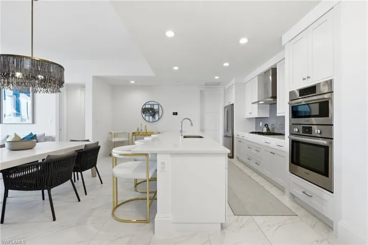 Gourmet kitchen featuring stainless steel appliances, white cabinetry, a large center island with a sink, quartz countertops, and marble-look tile flooring