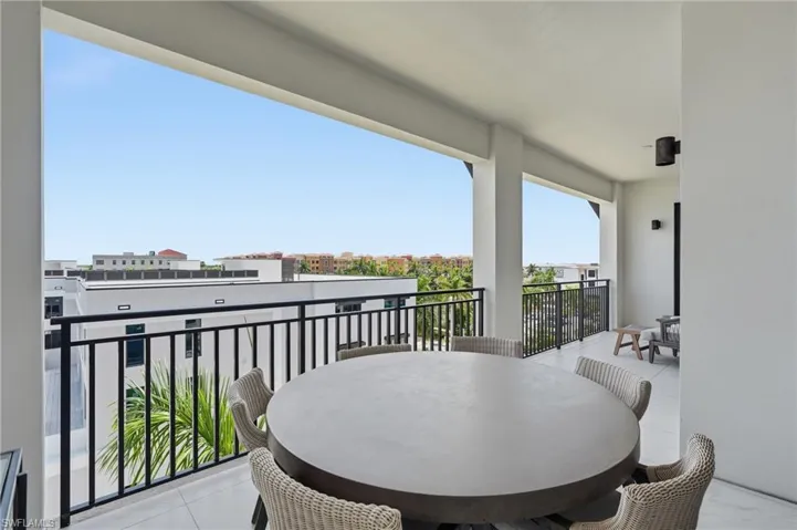 Covered balcony featuring white tile flooring, black metal railings, and dual exterior wall sconces