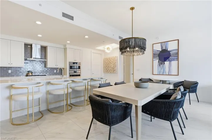 White shaker cabinetry with built-in stainless steel appliances, gray subway tile backsplash, and a breakfast bar with seating