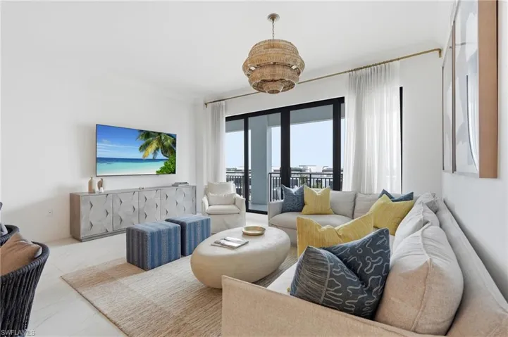 Open-concept living area with light-toned flooring, expansive glass doors, and a decorative woven chandelier