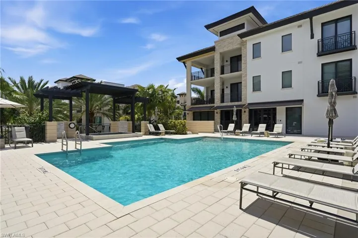 Resort-style swimming pool surrounded by paver decking, complete with sun loungers and a shaded pergola