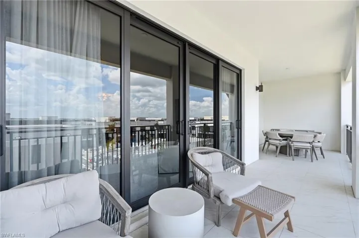 Expansive covered balcony featuring large sliding glass doors, a modern exterior light fixture, and tile flooring