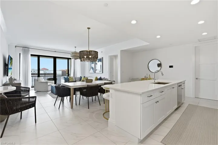 Open-concept living area with large format tile flooring, a kitchen island with integrated sink, recessed lighting, and expansive glass sliding doors