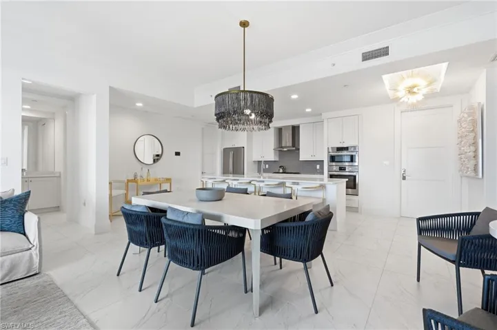 Open-concept dining and kitchen area featuring a light-filled space with white cabinetry, stainless steel appliances, quartz countertops, and a large island with seating