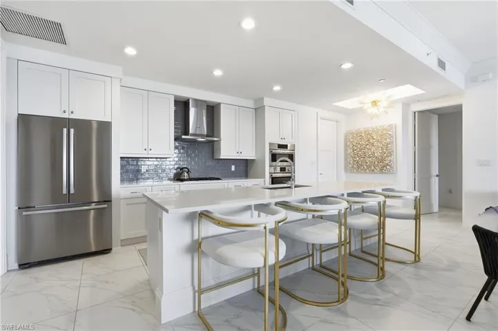 White cabinetry, stainless steel appliances, a center island with countertop seating, and recessed lighting