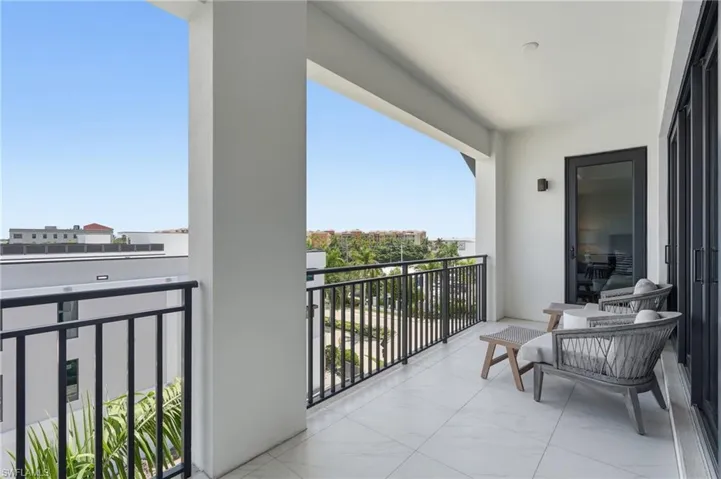 Expansive covered balcony featuring large format tile flooring, black metal railings, and a black framed glass door