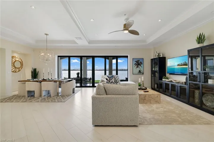Living area featuring a chandelier, light wood-style floors, ceiling fan, ornamental molding, and a tray ceiling