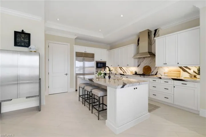 Kitchen featuring white cabinets, a breakfast bar, a kitchen island with sink, light stone countertops, and wall chimney exhaust hood