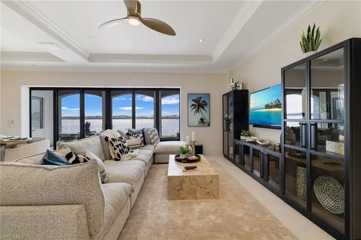 Living room with a raised ceiling, ceiling fan, ornamental molding, and recessed lighting