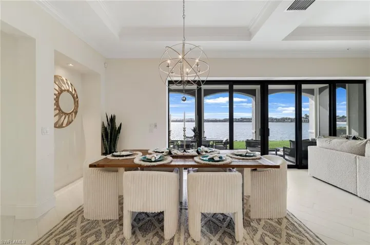 Dining room with a tray ceiling, a water view, a chandelier, and crown molding