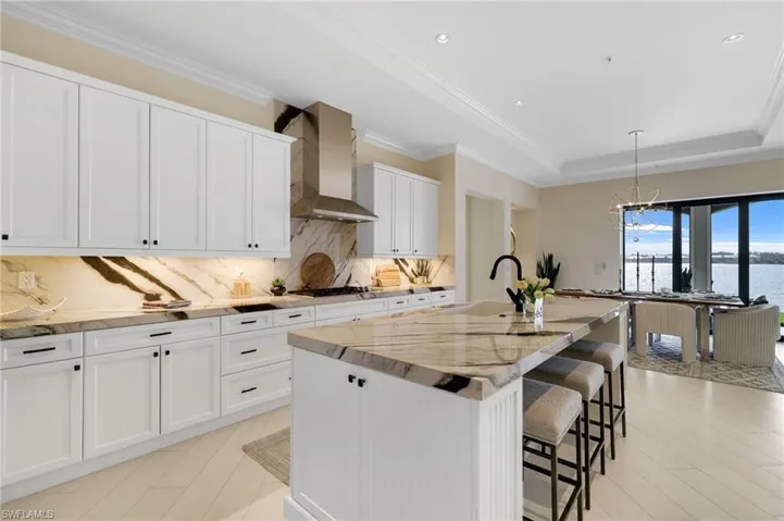 Kitchen with pendant lighting, white cabinets, a center island with sink, a breakfast bar area, and light stone countertops