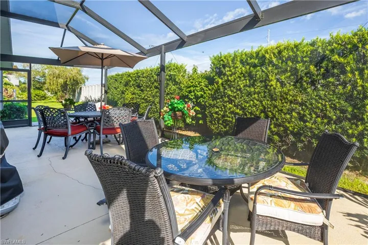 Screened patio with concrete flooring, framed by mature hedges