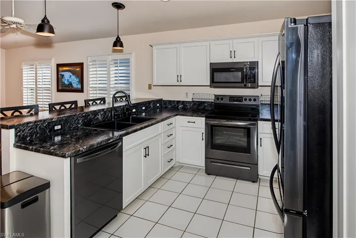 White cabinetry with black hardware, dark countertops, black sink with gooseneck faucet, white tiled flooring, and stainless steel appliances