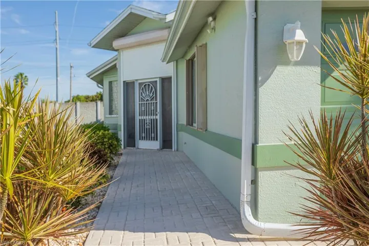 Stucco exterior with a contrasting trim, patterned paver walkway, and mature landscaping