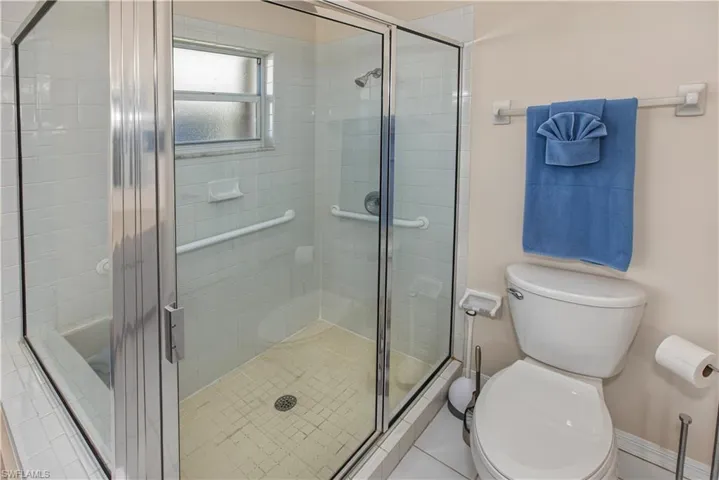 Glass-enclosed shower with a tiled surround, integrated grab bars, and a privacy window