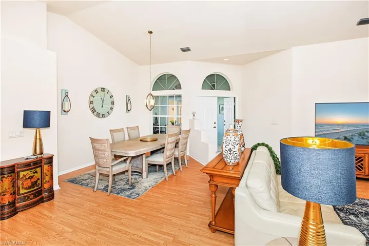 Vaulted ceiling with a pendant light fixture, wood-finish flooring, and arched window