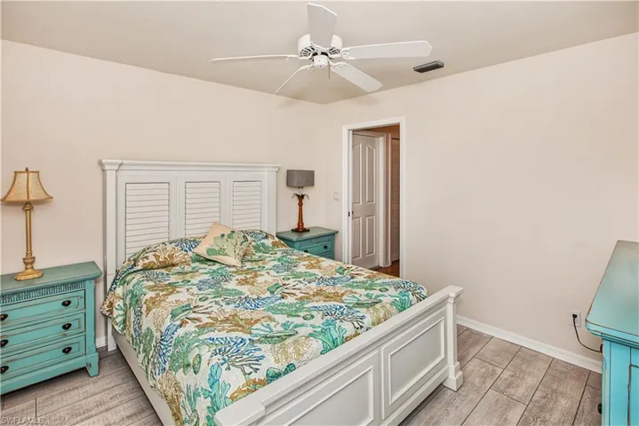 White louvered headboard, ceiling fan, and wood-finish flooring