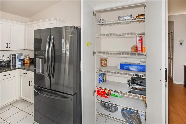 Modern kitchen featuring stainless steel French-door refrigerator with ice and water dispensers, white cabinetry with hardware accents, tile flooring, and a dedicated pantry with wire shelving offering ample storage for dry goods and kitchen essentials