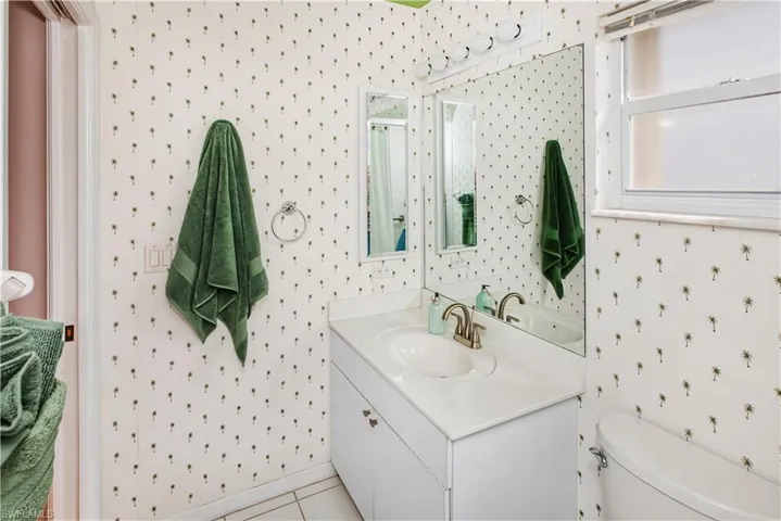 White vanity with integrated sink, brushed nickel faucet, large wall mirror, and overhead vanity lighting