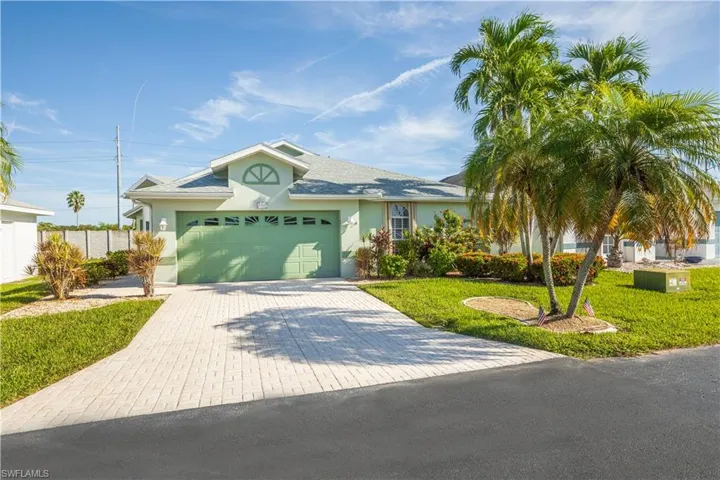Single-story residence featuring a light green exterior, an arched transom window, a green garage door, a paver driveway, and established palm trees