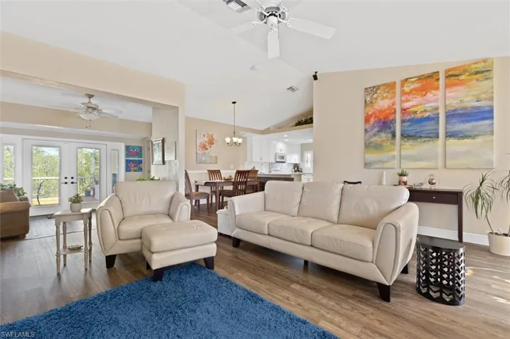 Living room featuring lofted ceiling, ceiling fan with notable chandelier, wood finished floors, baseboards, and french doors
