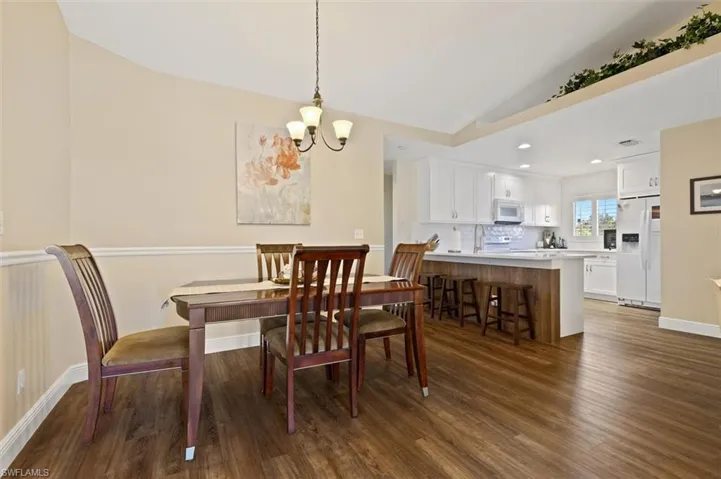 Dining area featuring baseboards, lofted ceiling, wood finished floors, a chandelier, and recessed lighting