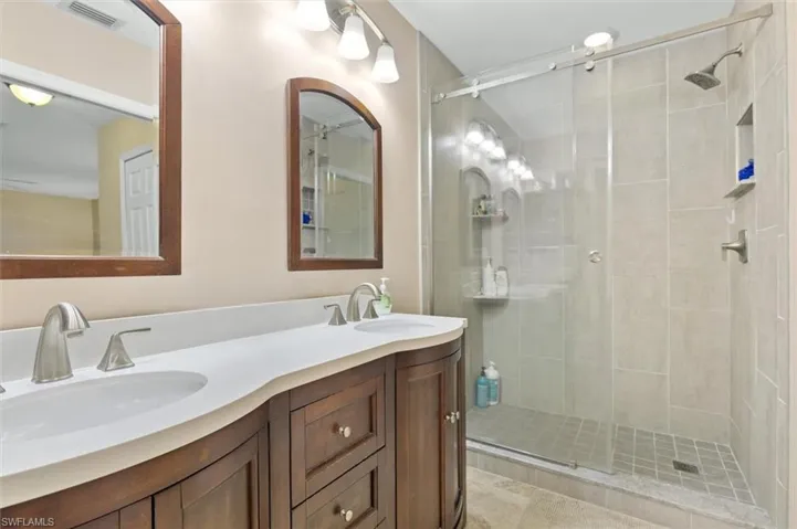 Full bath with double vanity, a sink, visible vents, and a shower stall