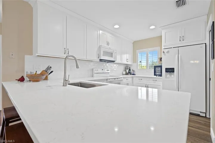 Kitchen featuring white appliances, light stone counters, a peninsula, white cabinetry, and a sink