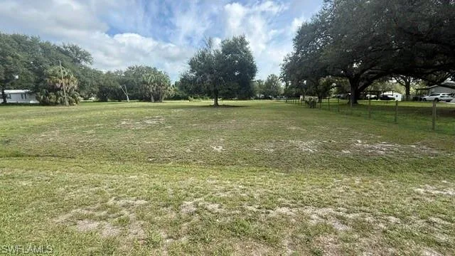 Expansive grass lot featuring mature trees and partial perimeter fencing